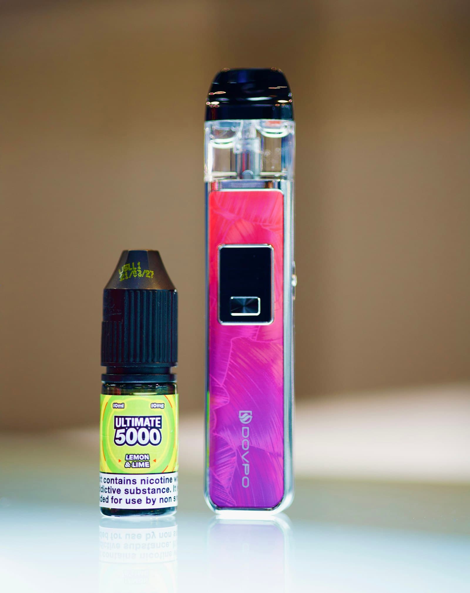 A pink pod vape kit standing next to a small 10ml e-liquid bottle on a plain background